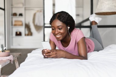 Kulaklık takan, yatak odasında müzik dinleyen siyah bir kadın.