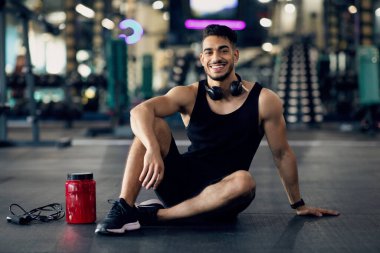 Beyaz Proteinli Konteynerin yanındaki spor salonunda oturan Arap erkek sporcu