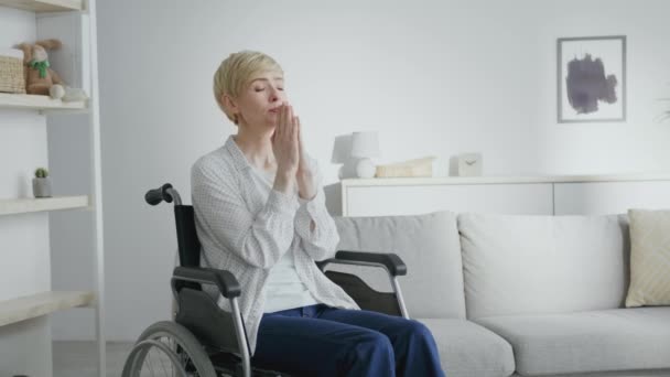 Femeia matură fără speranță cu leziuni ale coloanei vertebrale rugându-se lui Gao, stând în scaun cu rotile la domiciliu interior, spațiu gol — Videoclip de stoc