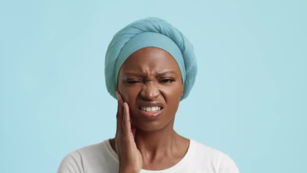 Mujer negra infeliz que sufre de dolor de muelas que toca la mejilla, fondo azul — Vídeos de Stock