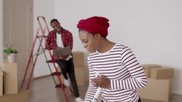 Siyah çift eve taşınıyor, kadın temizlik evi içeride eğleniyor. — Stok video