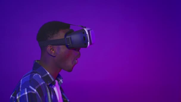 Geschokte Afrikaanse man dragen VR bril Kijkend opzij, Paarse achtergrond — Stockvideo