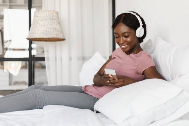 Yatak odasında cep telefonu kullanan Afro-Amerikalı kadın.