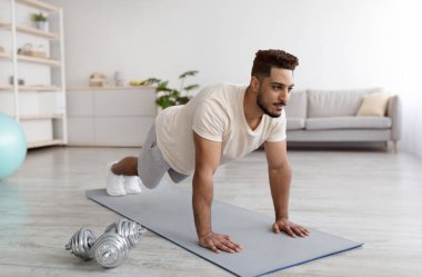 Genç Arap adam tahta duruşunda duruyor ya da şınav çekiyor, evde çalışıyor.