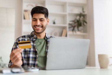 Gülümseyen genç adam bilgisayar ve kredi kartı kullanıyor, seçici odaklanma