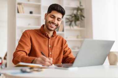 Laptop kullanan ve yazı yazan gülümseyen bir Arap portresi