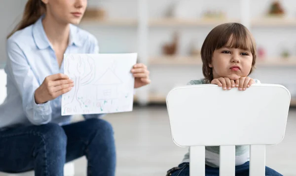 Παιδική κατάθλιψη. Αναστατωμένο αγόρι που κάθεται στην καρέκλα πίσω στον ψυχολόγο, γυναίκα που δείχνει εικόνα για ψυχική εξέταση, ελεύθερος χώρος — Φωτογραφία Αρχείου