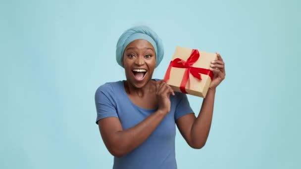 푸른 배경 위에 서 있는 즐거운 흑인 여인의 선물 상자 — 비디오