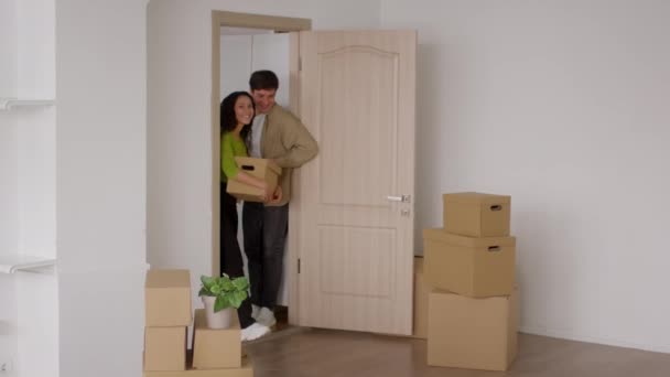Возбужденная пара входит в новый дом холдинг картон перемещения коробки в помещении — стоковое видео