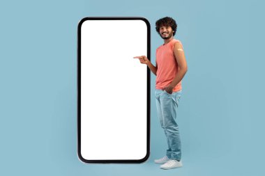Aşılanmış Hintli adam cep telefonunun beyaz ekranını işaret ediyor.