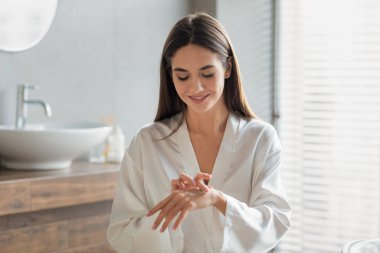 Beyaz ipek bornozlu güzel bayan ellerine süt sürüyor.