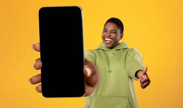 Szczęśliwa afrykańska, przerośnięta kobieta demonstrująca telefon komórkowy z pustym ekranem i z kciukiem w górze, makieta — Zdjęcie stockowe