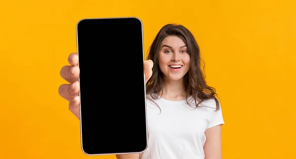 Wanita positif menampilkan ponsel besar dengan layar kosong, menunjukkan ruang bagi situs web Anda atau desain aplikasi — Stok Foto