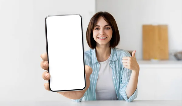Novo aplicativo. Senhora alegre mostrando smartphone com tela em branco no interior da cozinha, foco seletivo, mockup — Fotografia de Stock