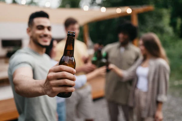 Çeşitli arkadaşları olan mutlu genç bir Arap adam bira şişeleriyle kadeh kaldırıyor, karavanın yanında alkol içiyor, seçici bir odak noktası var. — Stok fotoğraf