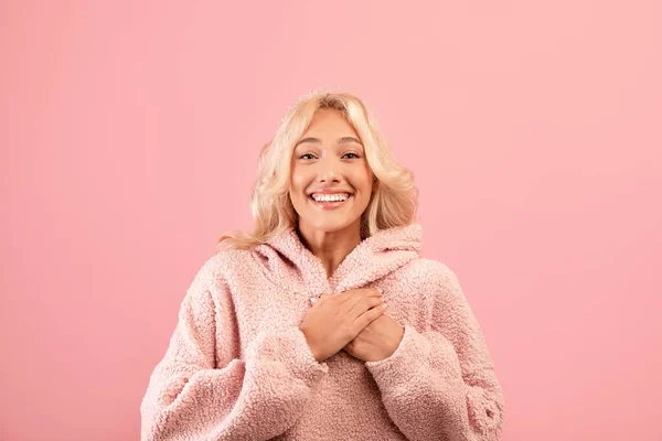 Tacksam dam håller händerna på bröstet, uttrycker tacksamhet, poserar över rosa studio bakgrund och ler mot kameran — Stockfoto
