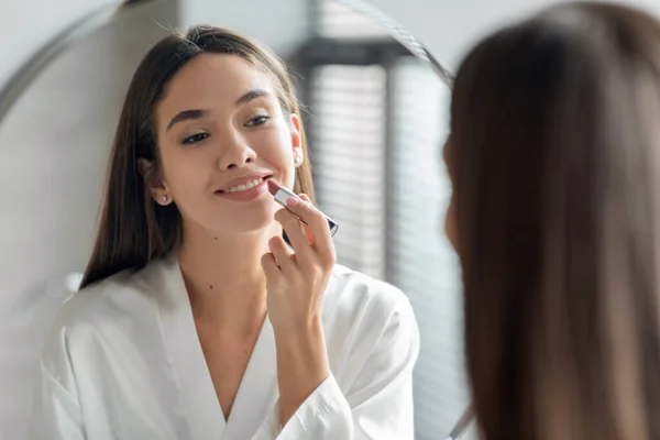 Rutina de maquillaje. Hermosa mujer joven aplicando lápiz labial desnudo en los labios cerca del espejo —  Fotos de Stock