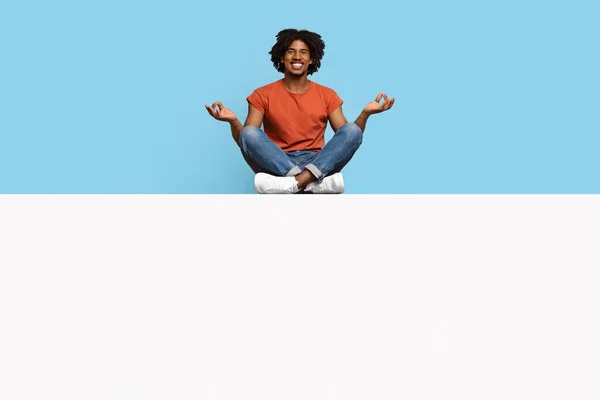 Chico negro alegre sentado en posición de loto en tablero vacío —  Fotos de Stock
