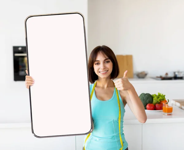 Glückliche junge, fitte Frau zeigt Handy mit leerem Bildschirm, gestikuliert Daumen hoch, empfiehlt Online-Schlankheits-App — Stockfoto