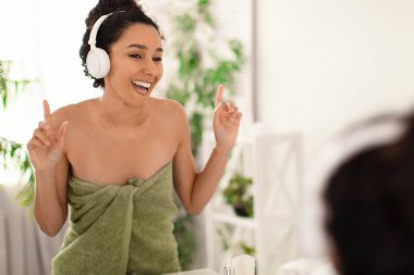 Kulaklık takmış, müzik dinleyen, dans eden, dans eden, şarkı söyleyen güzel bir kadın. Evdeki aynanın yanında.