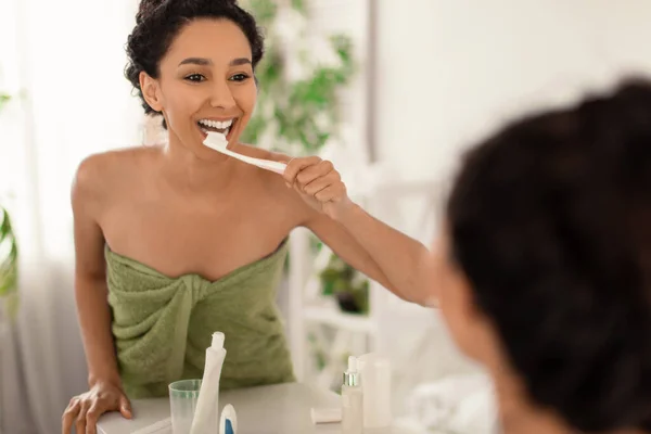 Стоматологія, поняття гігієни зубів. Красуня у рушнику чистить зуби зубною щіткою біля дзеркала вдома. — стокове фото