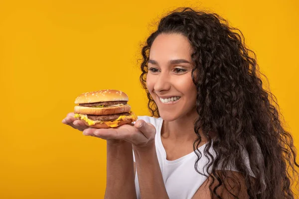 Divertida señora latina sosteniendo hamburguesa en el estudio — Foto de Stock