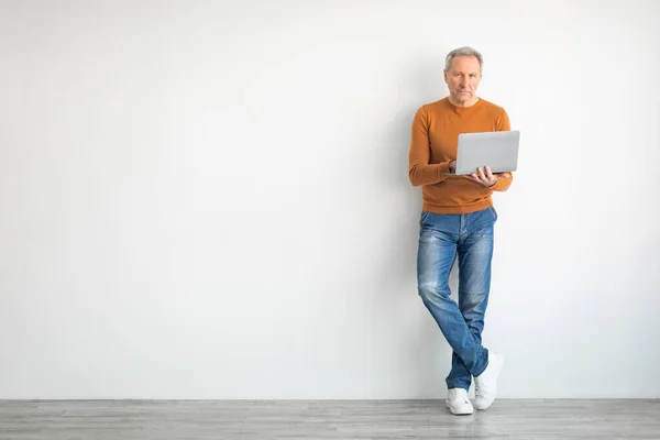 Magabiztos érett férfi laptoppal támaszkodik a falra — Stock Fotó