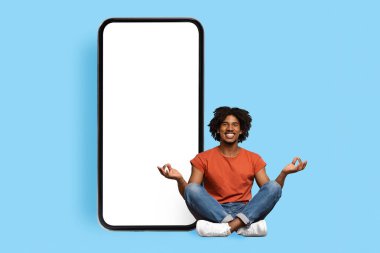 Huzurlu siyah adam büyük cep telefonunun yanında meditasyon yapıyor.