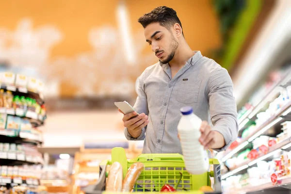 Arabic Guy Using Cellphone Holding Milk Buying Groceries In Supermarket — Stock Photo, Image