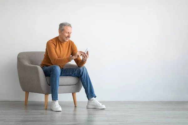 Portré érett férfi használ smartphone ül a karosszéken — Stock Fotó