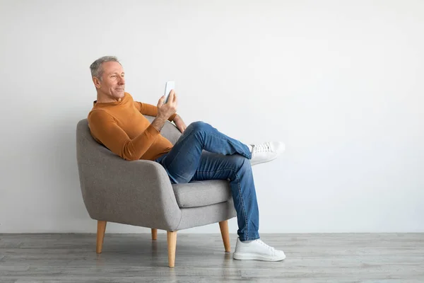 Akıllı telefon kullanan olgun bir adamın portresi koltukta oturuyor. — Stok fotoğraf