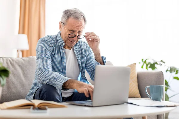 Ώριμος άντρας που αλληθωρίζει χρησιμοποιώντας φορητό υπολογιστή, κοιτάζοντας την οθόνη του υπολογιστή — Φωτογραφία Αρχείου