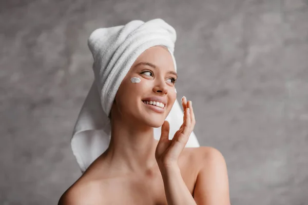 Szczęśliwy kaukaski kobieta stosując krem nawilżający pod oczami podczas wykonywania pielęgnacji skóry twarzy w łazience, przestrzeń kopiowania — Zdjęcie stockowe