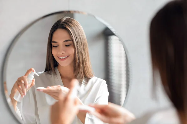 Jovem senhora atraente aplicando gel de limpeza em almofada de algodão perto do espelho — Fotografia de Stock