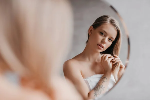 Természetes szépség. Csinos fiatal hölgy megérinti a puha haját, közel áll a tükörhöz a fürdőszobában, és nézi a tükörképét — Stock Fotó
