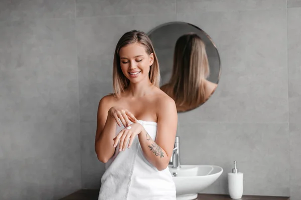 Šťastná dáma pomocí hydratační krém na ruce, tření vyživující tělové mléko na ruce, sedí v koupelně — Stock fotografie