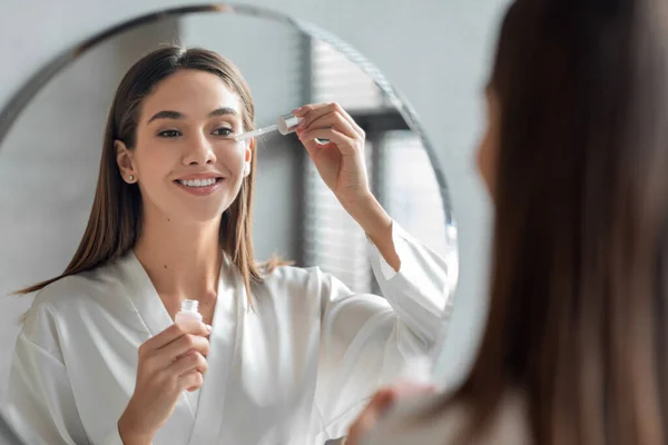 Skin Care Concept. Indah Milenial Woman Menerapkan Wajah Serum Dekat Cermin — Stok Foto