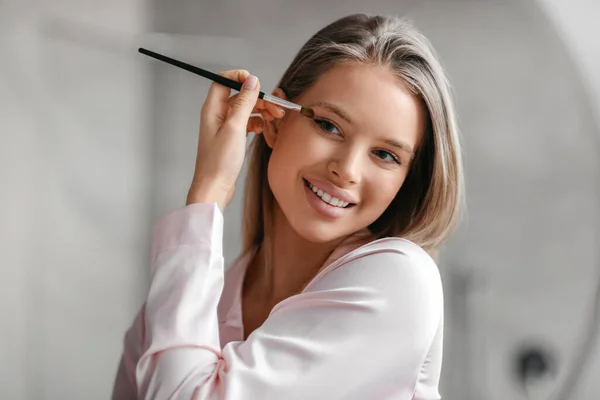 Sensual senhora aplicando sombra olho com aplicador perto do espelho no interior do banheiro, usando produto cosmético orgânico — Fotografia de Stock