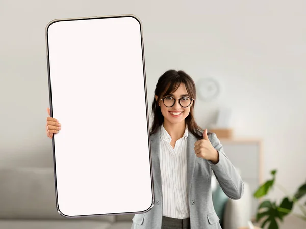 Jovem empresária feliz mostrando gesto polegar para cima, demonstrando celular com mockup para site ou aplicativo móvel — Fotografia de Stock