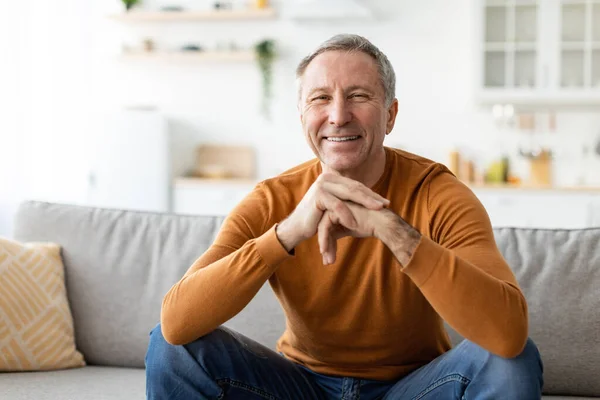 Smiling mature man sitting on the couch and posing — Stock Photo, Image