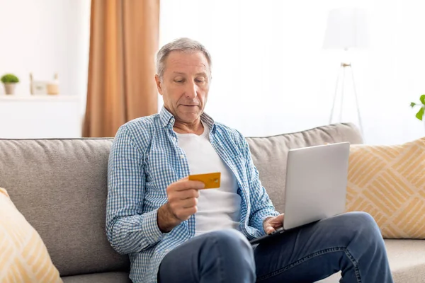 Εστιασμένη ώριμος άνθρωπος χρησιμοποιώντας υπολογιστή και πιστωτική κάρτα στο σπίτι — Φωτογραφία Αρχείου