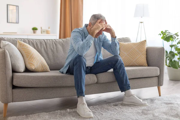 Estressado maduro homem sentado no sofá agarrando cabeça — Fotografia de Stock