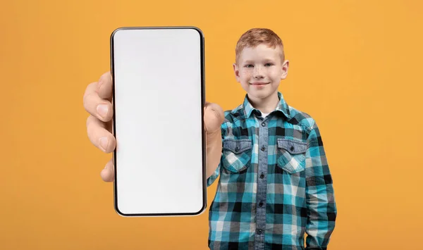 Souriant rousse garçon démontrant grand smartphone avec écran blanc vierge à la caméra — Photo