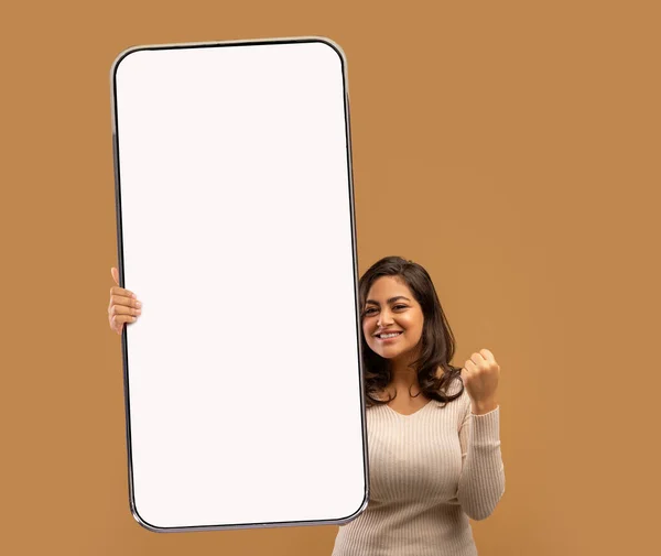 Привлекательная молодая арабская женщина, жестикулирующая ДА, держащая большой телефон с пустым экраном на бежевом фоне, макет — стоковое фото