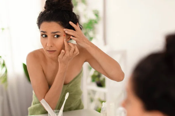 Jeune femme bouleversée se regardant dans un miroir, vérifiant l'acné sur son visage à la maison, espace de copie — Photo