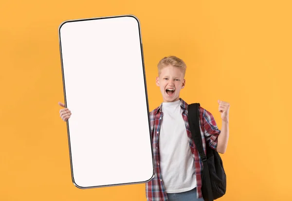 Nadšený školák s batohem dělá YES gesto, ukazuje mobilní telefon s maketou pro elearning app design — Stock fotografie