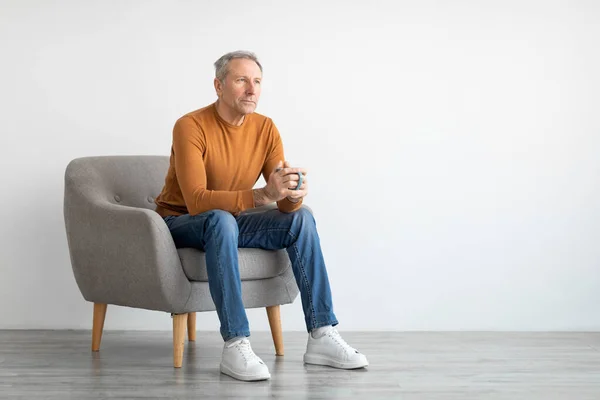 Adam evde dinleniyor, sandalyeye oturuyor, kahve içiyor. — Stok fotoğraf