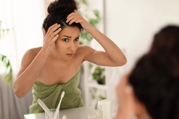 Wanita Milenial yang prihatin memiliki masalah ketombe atau masalah rambut abu-abu, melihat akarnya di cermin di kamar mandi — Stok Foto