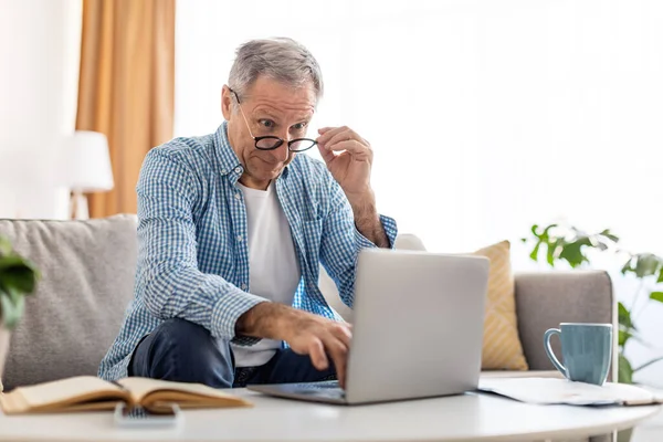 Überraschter älterer Mann benutzt Laptop und schaut auf Bildschirm — Stockfoto