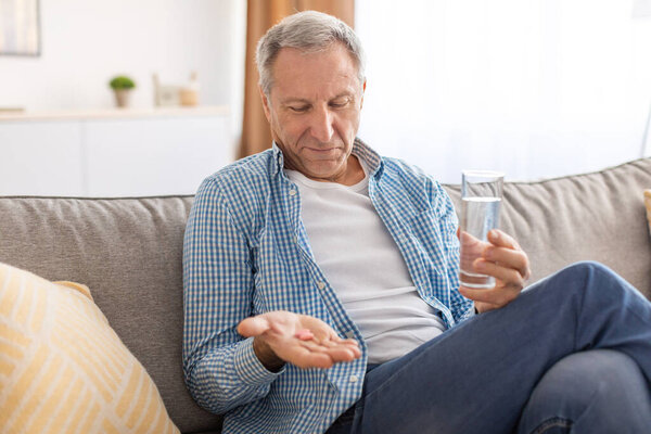 Mature man taking pills holding glass of water